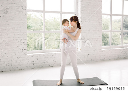 Portrait of beautiful young mom in sports wear holding her charming little baby, standing on black Portrait of beautiful young mom in sports wear holding her charming little baby, standing on black 59169056
