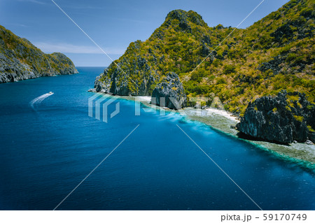 Limestone karst coastline of Matinloc Island with tourist boats in ocean strait. El Nido, Palawan 59170749