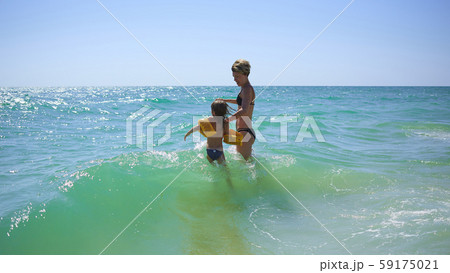 Summer happy family of six years blonde child playing and jumping water waves embracing woman mother 59175021