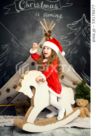 Little girl in Santa costume on a rocking horse is Little girl in Santa costume on a rocking horse is 59176677