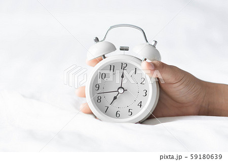 Closeup hand holding alarm clock on white bed Closeup hand holding alarm clock on white bed 59180639
