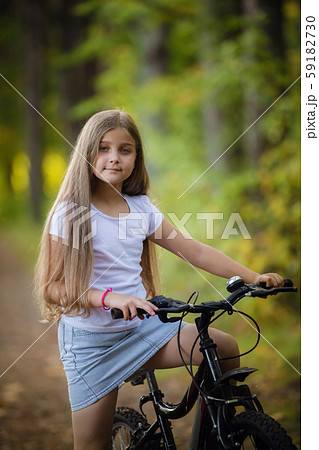 Cute little teenager girl riding bicycle in a sunny park 59182730