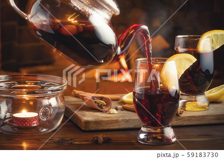 Pouring mulled wine into glasses from a teapot in a room with a fireplace 59183730