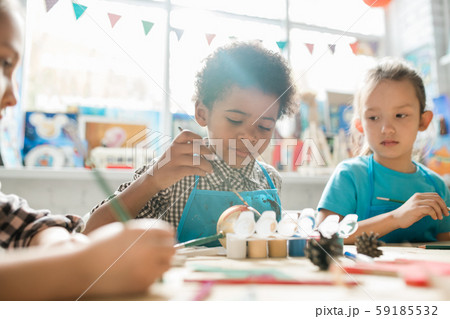 Serious schoolboy and his classmate painting Christmas decorations by desk 59185532