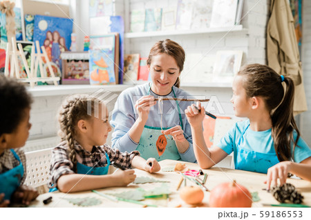 Happy young teacher showing group of schoolkids halloween pumpkin decoration 59186553