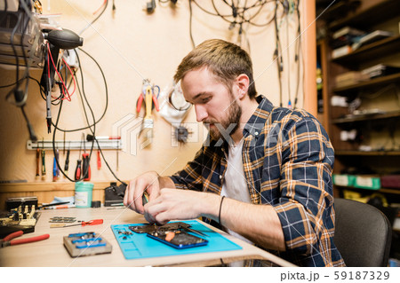 Professional repairman bending over broken smartphone and fixing tiny details Professional repairman bending over broken smartphone and fixing tiny details 59187329