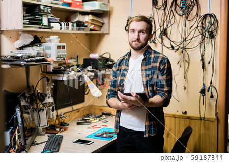 Young successful master in casualwear holding one of broken gadgets Young successful master in casualwear holding one of broken gadgets 59187344