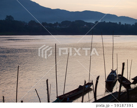 relax background scene of evening sunlight on river bank with rural primitive vintage retro style fisherman's boats silhouette on smooth water surface at MEKONG RIVER in LUANG PRABANG province, LAOS relax background scene of evening sunlight on river bank with rural primitive vintage retro style fisherman's boats silhouette on smooth water surface at MEKONG RIVER in LUANG PRABANG province, LAOS 59187391