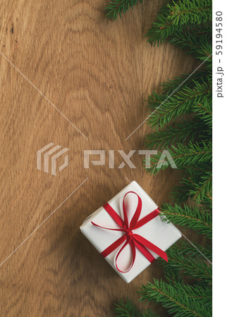 Flat lay christmas background with spruce twigs and white gift box with red ribbon on oak wood 59194580