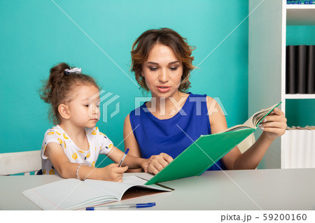 Daughter with mother sitting at the table together and doing homework. 59200160