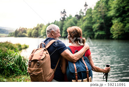 Rear view of senior tourist couple on a walk in nature, standing by lake. 59211091