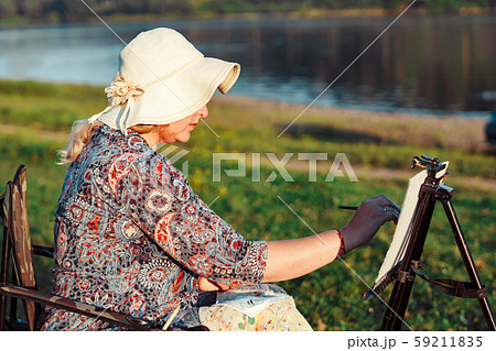 an elderly woman paints a picture in nature 59211835