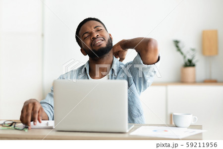 Black man suffering from neck pain while working on laptop 59211956