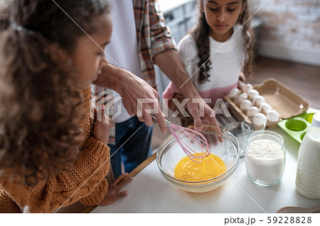 Girls watching their father whipping eggs while cooking pie 59228828