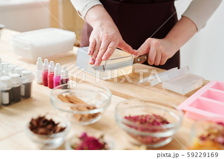 Hands of craftswoman with knife cutting piece from large bar of hard soap mass Hands of craftswoman with knife cutting piece from large bar of hard soap mass 59229169
