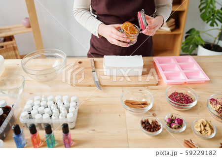 Girl opening small jar with dry orange slices to put them into liquid soap mass 59229182