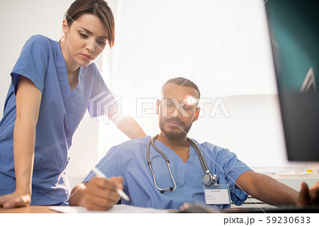 One of young clinicians showing his notes to colleague during discussion One of young clinicians showing his notes to colleague during discussion 59230633