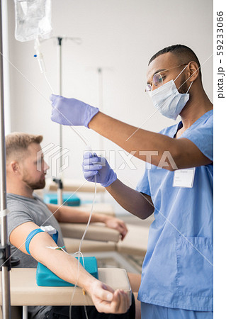 Intern in uniform, protective mask and gloves preparing dropper for patient Intern in uniform, protective mask and gloves preparing dropper for patient 59233066