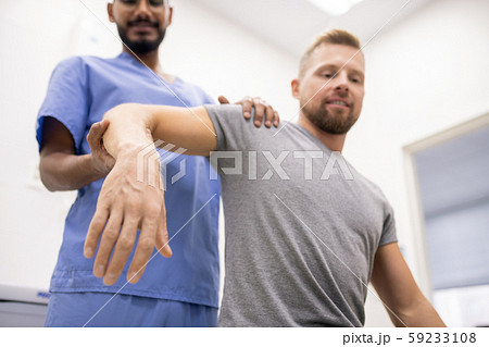 Masseur in blue uniform holding sick arm of patient while massaging it 59233108