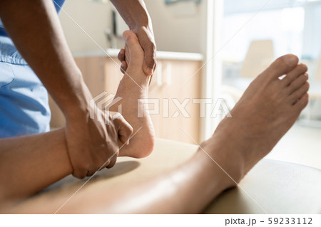 Hands of young mixed-race medical professional massaging one of feet of patient 59233112