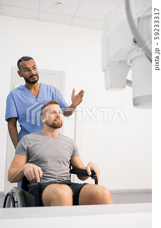Doctor in blue uniform showing patient on wheelchair new medical equipment Doctor in blue uniform showing patient on wheelchair new medical equipment 59233317