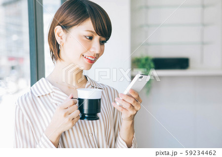 仕事の休憩中にスマホを見ながらコーヒーを飲む女性 59234462