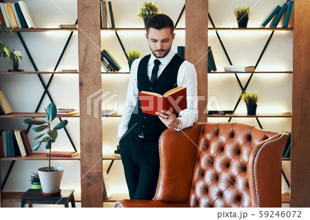 Handsome young man in elegant suit reading a book in modern luxury interior 59246072