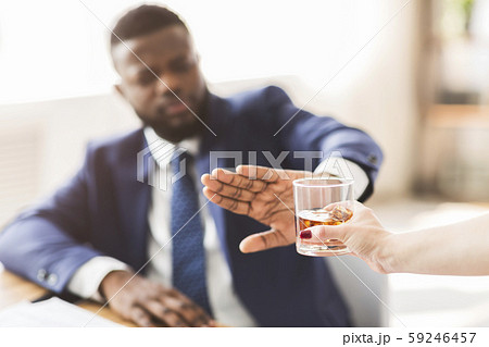 Businessman saying no to glass of whiskey offered by colleague 59246457