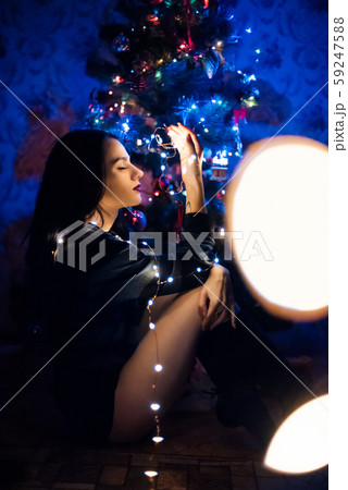 pretty girl is sitting on the background of a festive Christmas tree with a garland pretty girl is sitting on the background of a festive Christmas tree with a garland 59247588