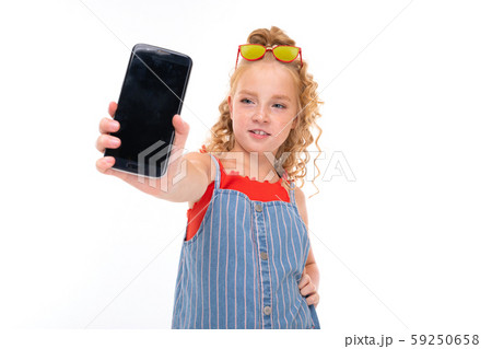 Picture of happy child with fair red curly hair shows a phone isolated on white backround 59250658