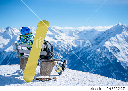 Image from back of athlete man sitting on bench next to snowboard in ski resort. 59255207