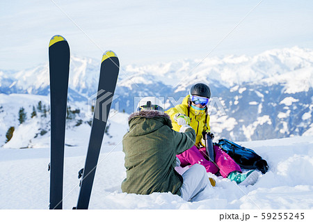 Photo of skis against background of two sports women with thermos sitting in ski resort in winter in Photo of skis against background of two sports women with thermos sitting in ski resort in winter in 59255245