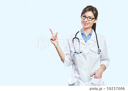 Friendly smiling young female doctor. hand pointing at copy space. isolated on a light blue 59257006
