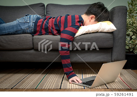 An asian smart looking preteen - teenager boy lying face down, exhausted, frustrated on the couch, browsing his social media on laptop computer. Teen problem, Cyber bullying, Laziness, Digital device. An asian smart looking preteen - teenager boy lying face down, exhausted, frustrated on the couch, browsing his social media on laptop computer. Teen problem, Cyber bullying, Laziness, Digital device. 59261491