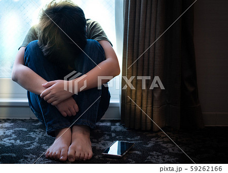 Portrait of a teenager boy sitting alone in the room with his smartphone, feeling hurt, anxiety and depress from Cyber bullies on social media. Technology cause teens mental health problems concept. 59262166