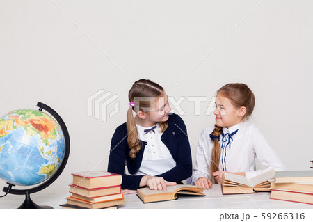 two schoolgirl girls with books and a globe in class at the desk two schoolgirl girls with books and a globe in class at the desk 59266316