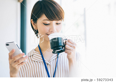 仕事の休憩中にスマホを見ながらコーヒーを飲む女性 59273343