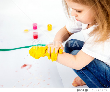 pretty child girl smears yellow paint on hands pretty child girl smears yellow paint on hands 59278529