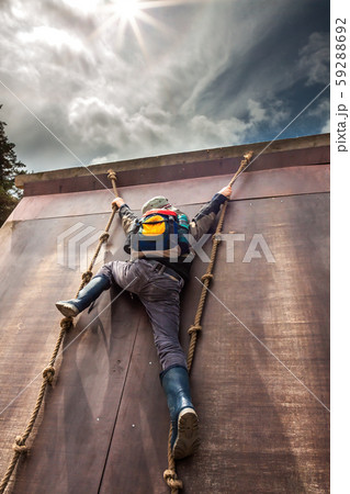 Young boy in wellys climbing up a wall with ropes Young boy in wellys climbing up a wall with ropes 59288692