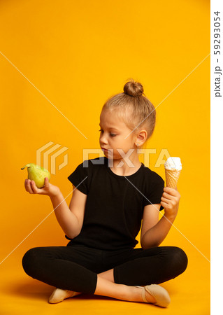 Cute little blonde girl choosing between pear and sweet ice-cream on yellow background Cute little blonde girl choosing between pear and sweet ice-cream on yellow background 59293054