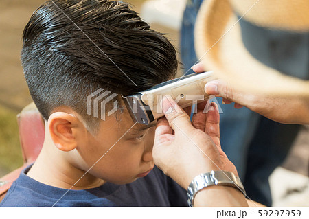 Closeup face of a good looking young asian teenager boy getting a haircut by a barber, hairdresser's hand with electric clipper neatly trim for sharp look and the style. Professional haircut, Handsome 59297959