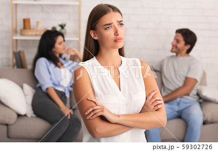 Offended Girl Standing While Boyfriend Flirting With Girl Sitting Indoor 59302726