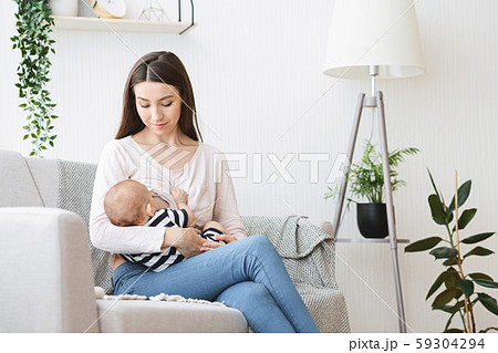 Beautiful young mother breastfeeding her baby on couch at home 59304294