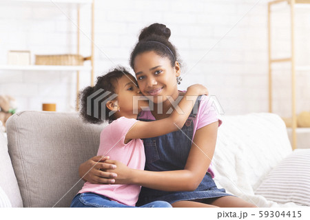 Little african girl kissing her elder sister at home Little african girl kissing her elder sister at home 59304415