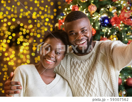 Happy black couple making selfie with Christmas tree on background Happy black couple making selfie with Christmas tree on background 59307562