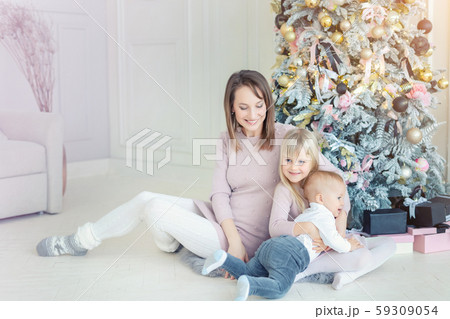 Portrait of cute adorable little blond children with mother enjoy sitting near christmas tree in 59309054