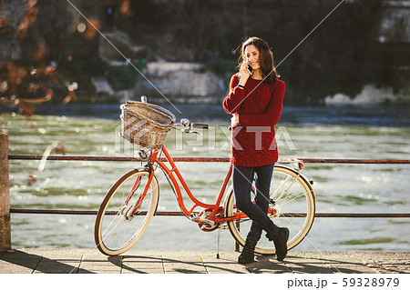 A young female traveler enjoying stands next to a bicycle near a river in the city of Basel 59328979
