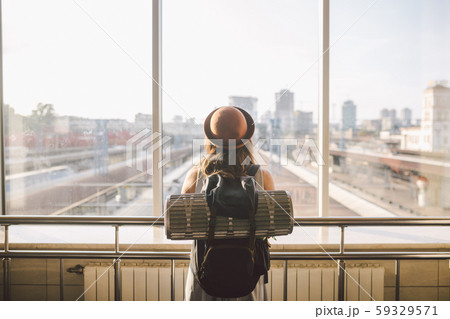 Traveler Rear view woman standing at the window in hall Train Station departure with backpack 59329571