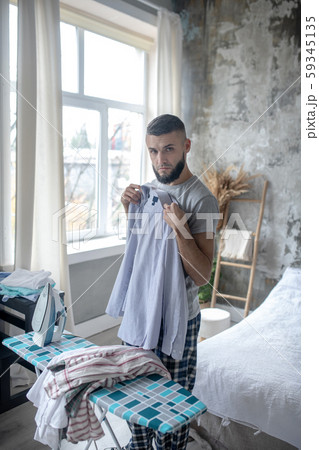 Serious dark-haired man ironing shirt in the bedroom Serious dark-haired man ironing shirt in the bedroom 59345135