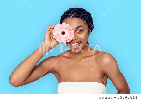 Beauty Concept. Young african woman isolated on blue covering eye with flower smiling playful 59345811